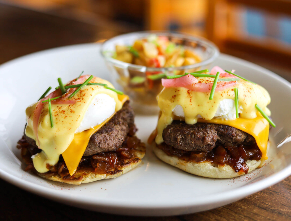 Two extra-large poached eggs, Gyulais Wagyu patty, toasted English muffin, American cheese, TX® bacon jam, cayenne citrus hollandaise, pickled onions, chives, paprika, choice of stone-ground yellow grits or house potatoes