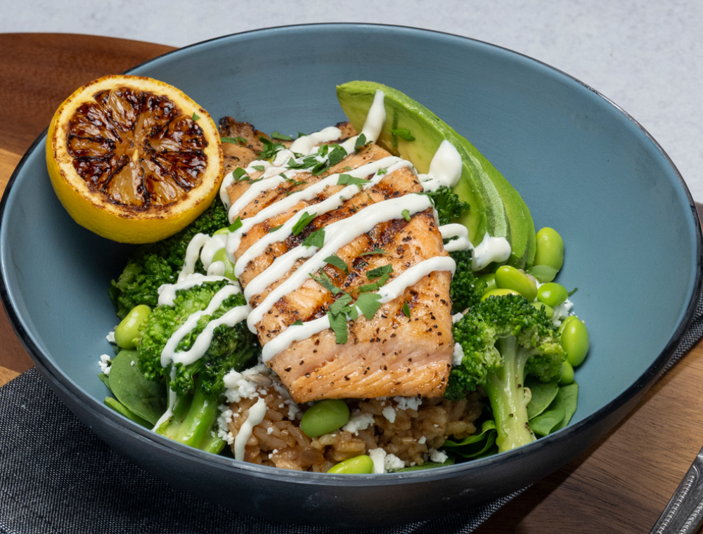 Atlantic salmon fillet, sesame soy garlic rice, spinach, broccoli, feta, edamame, sunflower seeds, avocado, lemon dill crema, charred lemon <br>60 grams of protein
