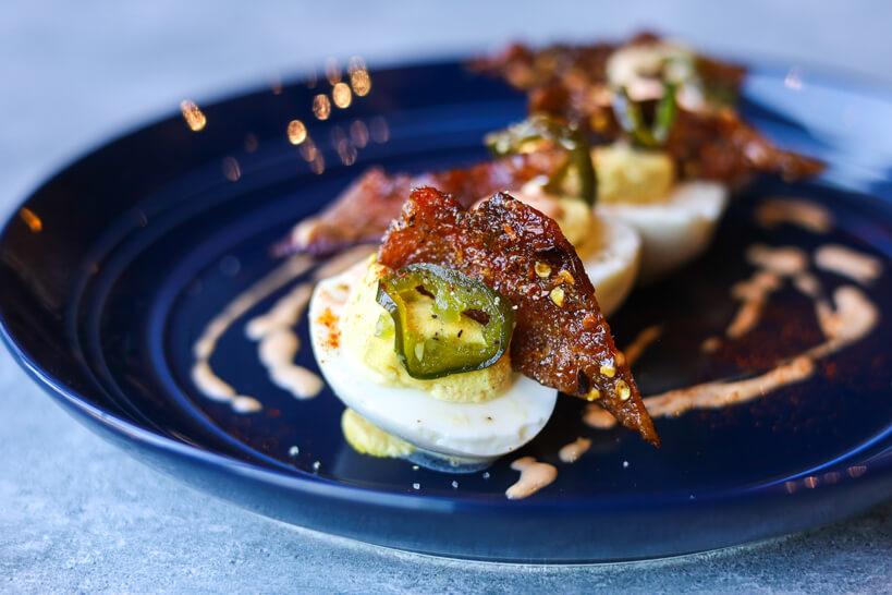 Deviled Eggs topped with candied jalapeños, candied bacon, hot sauce mayo and paprika